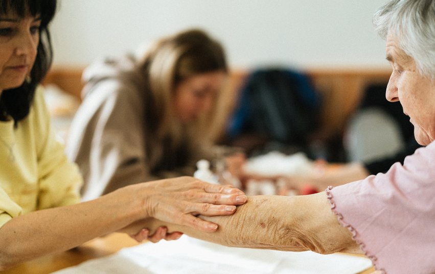 Pečovatelka natírá ruku seniorce